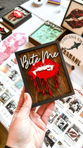 Load image into Gallery viewer, Bite Me Shelf Sign - FireDrake Artistry® wooden sign with natural background, dark grey frams, white "Bite Me" wording and red vampire lips.
